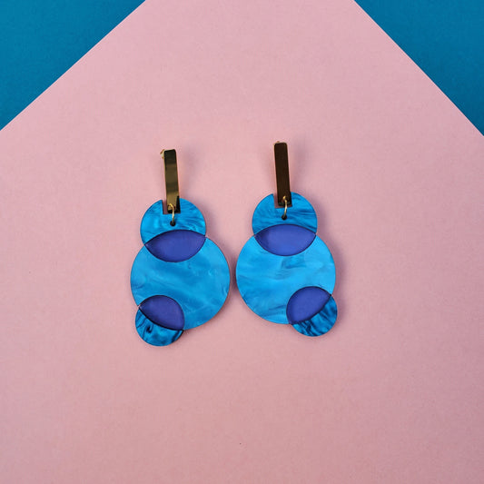 Earrings are made entirely out of acrylic with a golden stainless-steel hook. They are 3" long and weigh .20 lbs. The earrings are made with blue acrylic combined with blue translucent acrylic to emphasize the union between the 3 circles.